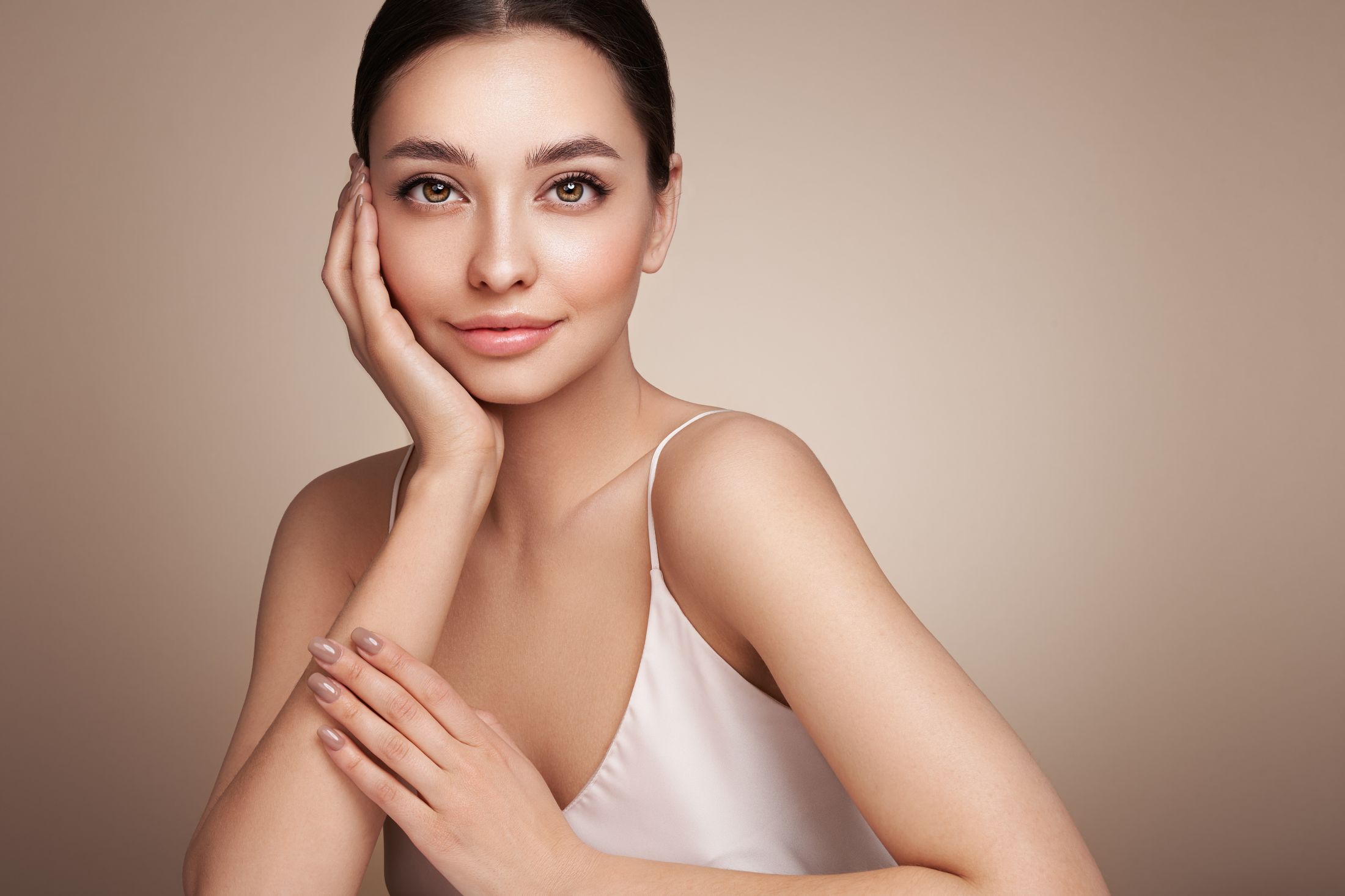 Woman with natural makeup, elegant hairstyle, neutral background.